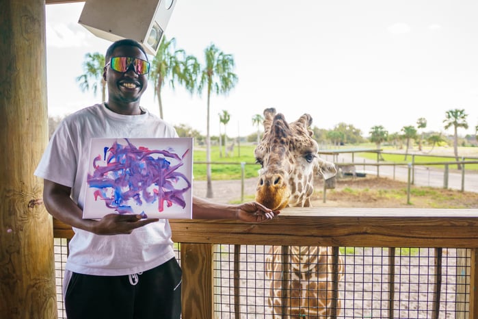 Guest holding artwork made during the Giraffe Painting Experience at Wild Florida Drive-thru Safari Park